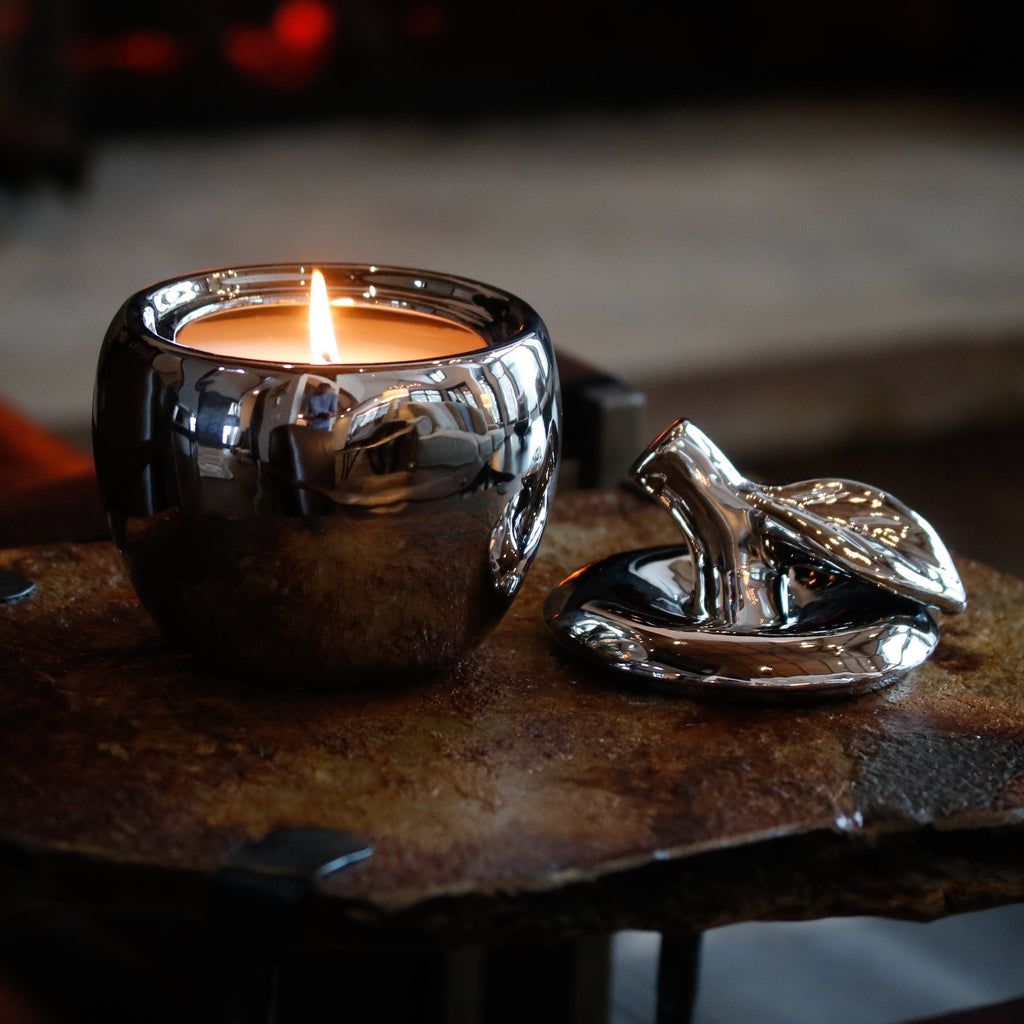 silver apple shaped candle with a single lit cotton wick