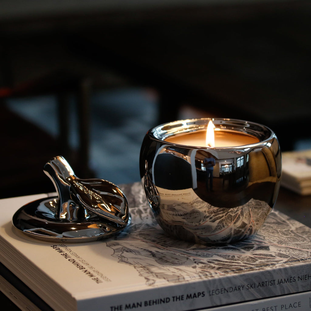 silver ceramic apple candle with a single lit cotton wick